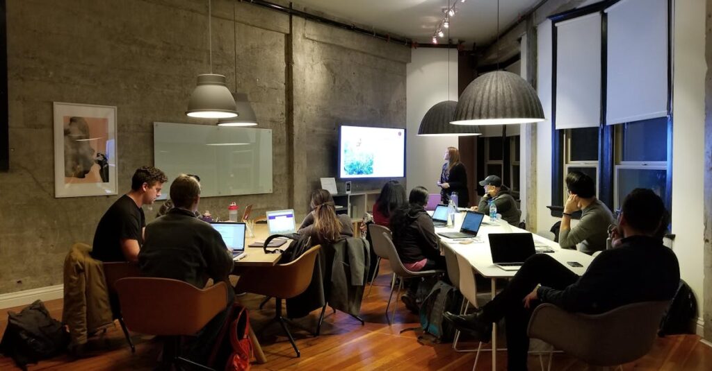 Diverse team collaborating in a modern office setting with laptops and presentation screen.